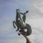 Outdoor bronze statue of a horse and rider under a cloudy sky, showcasing movement and heritage.